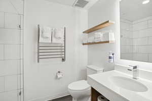 Bathroom featuring vanity, toilet, visible vents, radiator heating unit, and a shower