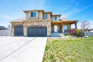 View of front of house with a porch, fence, driveway, stone siding, and a front yard