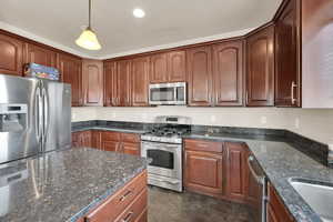 Kitchen with dark stone counters, dark tile patterned floors, stainless steel appliances, a sink, and pendant lighting