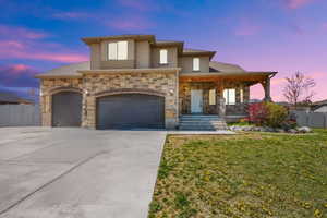 View of front of home with a porch, a yard, fence, driveway, and stone siding
