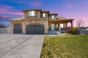 View of front of house with fence, concrete driveway, stone siding, covered porch, and a lawn