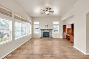 Unfurnished living room featuring light wood-type flooring, a ceiling fan, visible vents, and a fireplace