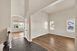 Empty room with visible vents, arched walkways, baseboards, a towering ceiling, and dark tile patterned flooring