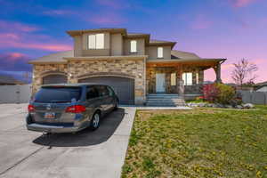 View of front of house with covered porch, fence, stone siding, a front lawn, and concrete driveway
