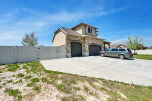 View of side of home with stucco siding, a gate, fence, driveway, and stone siding