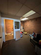 Interior space featuring a drop ceiling, carpet flooring, and brick wall