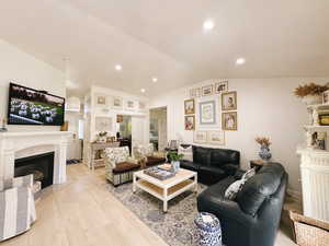 Living room with light wood-type flooring, a premium fireplace, vaulted ceiling, and recessed lighting