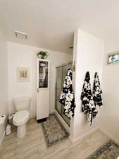 Full bath with toilet, visible vents, a textured ceiling, and a stall shower