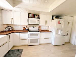 Kitchen with tasteful backsplash, wood counters, white appliances, light wood finished floors, and white cabinets