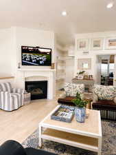 Living area featuring baseboards, a glass covered fireplace, wood finished floors, and recessed lighting