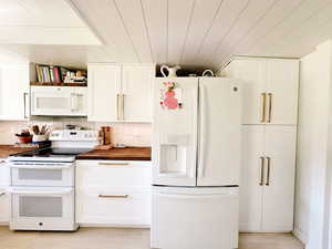 Kitchen with butcher block countertops, white cabinets, and white appliances