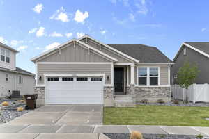 Craftsman house with concrete driveway, board and batten siding, stone siding, fence, and a front lawn