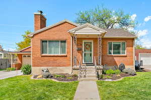 Bungalow-style house with a front yard, a chimney, a garage, and brick siding