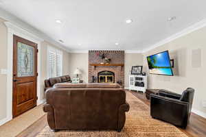Living room with ornamental molding, a brick fireplace, wood finished floors, and recessed lighting
