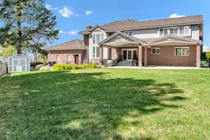 Rear view of house featuring brick siding, a lawn, an outbuilding, and a storage shed