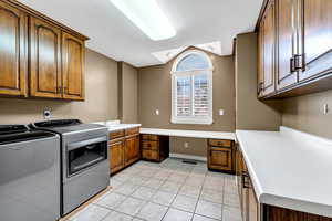 Clothes washing area featuring washing machine and clothes dryer, a sink, light tile patterned floors, cabinet space, and visible vents