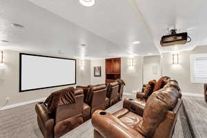 Home theater room featuring baseboards, a textured ceiling, and light colored carpet