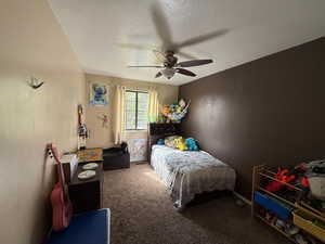 Bedroom with a ceiling fan, carpet floors, and a textured ceiling