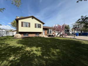 Back of property featuring a chimney, brick siding, fence, entry steps, and a lawn