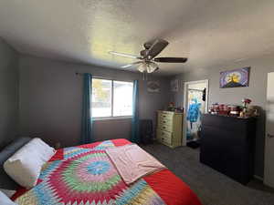 Bedroom featuring a ceiling fan, dark carpet, and a textured ceiling
