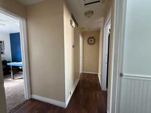 Hall with baseboards, visible vents, attic access, and dark wood-style flooring