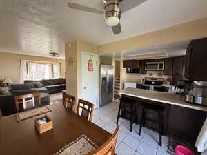 Dining space with light tile patterned flooring, ceiling fan, stairway, and a textured ceiling