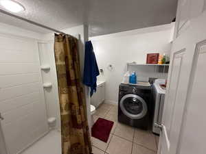 Bathroom featuring curtained shower, washer and dryer, tile patterned floors, and a textured ceiling