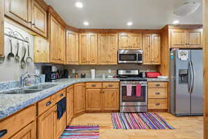 Kitchen with light wood-style flooring, light stone countertops, a sink, and appliances with stainless steel finishes