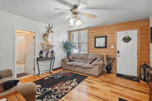 Living area with a textured ceiling, rustic walls, light wood-style floors, ceiling fan, and visible vents