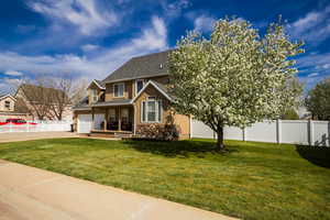 View of front of house featuring fence, stone siding, roof with shingles, a front lawn, and concrete driveway