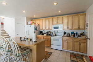 Kitchen with light tile patterned floors, a sink, a kitchen bar, white appliances, and a center island with sink