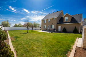 Rear view of house featuring a lawn, roof with shingles, a patio, and a fenced backyard