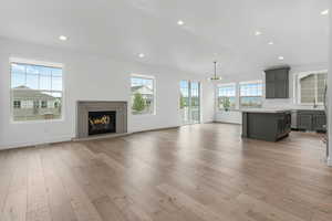 Unfurnished living room featuring baseboards, a notable chandelier, light wood-style floors, and a glass covered fireplace