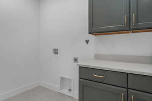 Washroom featuring hookup for an electric dryer, hookup for a washing machine, cabinet space, and baseboards