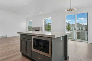Kitchen featuring lofted ceiling, stainless steel microwave, light wood-style flooring, visible vents, and an inviting chandelier