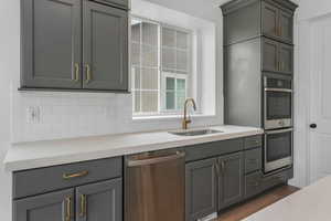 Kitchen featuring gray cabinetry, a sink, backsplash, and stainless steel appliances