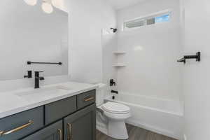 Bathroom featuring toilet, shower / bathtub combination, wood finished floors, and vanity
