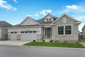 Craftsman house with board and batten siding, a garage, driveway, stone siding, and a front lawn