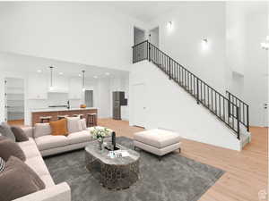 Living area featuring stairs, light wood-type flooring, baseboards, visible vents, and a high ceiling