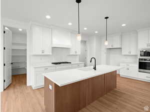 Kitchen with light wood-style flooring, custom range hood, a sink, black stovetop, and stainless steel oven