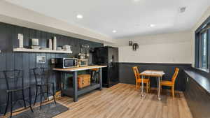 Kitchen featuring recessed lighting, wood finished floors, stainless steel microwave, wooden walls, and black fridge