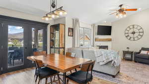 Dining area featuring light wood finished floors, lofted ceiling, a glass covered fireplace, a ceiling fan, and french doors