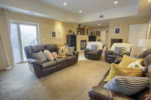 Carpeted living room featuring a glass covered fireplace, visible vents, and recessed lighting