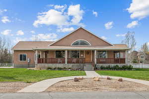 View of front of home with a porch, a front yard, stucco siding, and fence