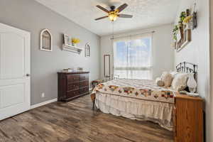 Bedroom featuring ceiling fan, baseboards, a textured ceiling, and dark wood-style floors