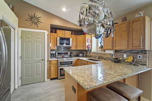 Kitchen featuring tasteful backsplash, light stone countertops, appliances with stainless steel finishes, a sink, and a peninsula