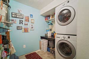 Washroom with a textured ceiling, stacked washer / drying machine, and laundry area