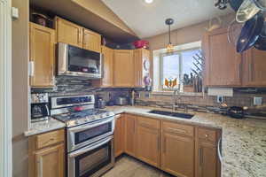 Kitchen featuring light stone countertops, stainless steel appliances, backsplash, a sink, and lofted ceiling