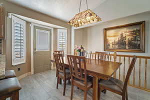 Dining room featuring a textured ceiling, plenty of natural light, a notable chandelier, and baseboards