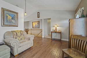 Living area featuring wood finished floors, visible vents, vaulted ceiling, and baseboards